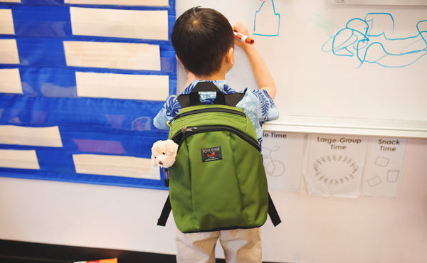 A child drawing on a white-erase board while wearing The Sprout.
